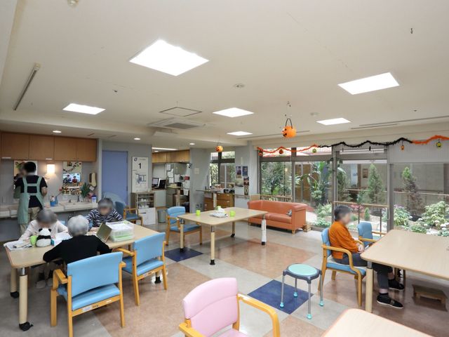 広々とした明るいダイニング 食堂兼談話室 天井の高い開放感あふれるダイニングルームです。利用者様が明るく広い空間で憩いの時間を過ごされています。