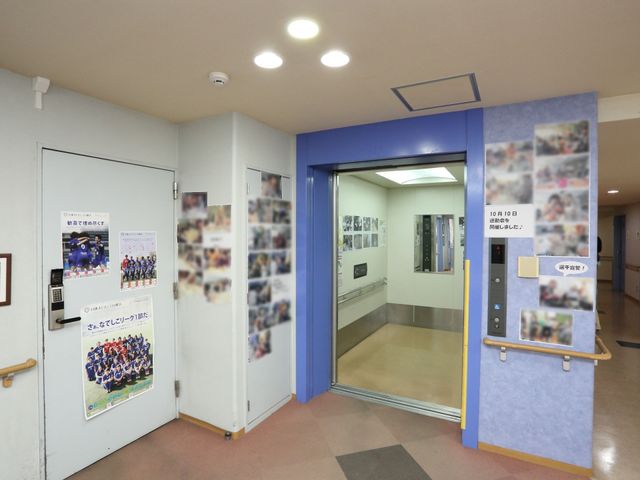廊下の自動ドアと掲示物 エレベーター 自動式の入口はアクセスが容易で、イベントの掲示物が周囲に飾られており、活気ある雰囲気を感じさせる空間です。