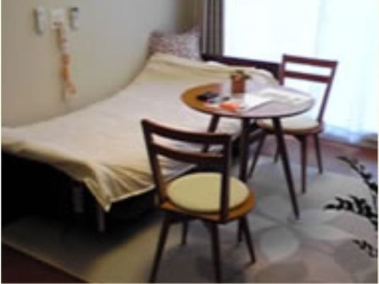 居室にはベッドが置かれており、壁側には呼び出しボタンが設置されている。ベッドの近くには丸いテーブルと椅子2脚が用意されている。