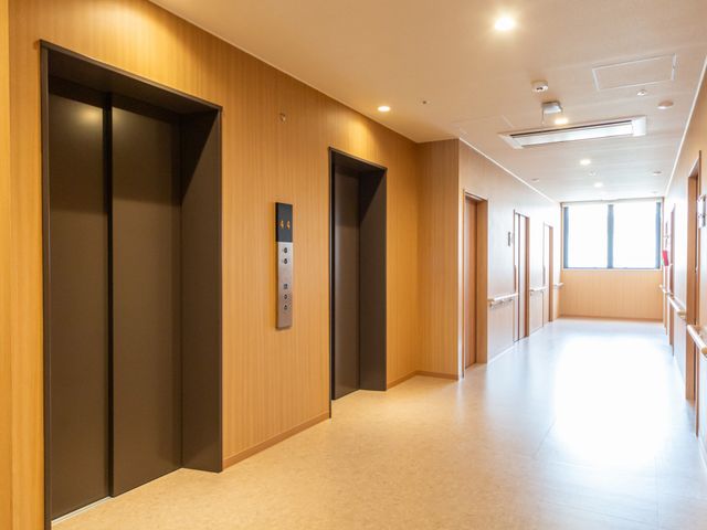 明るい廊下とエレベーター 廊下   木目調で統一された廊下にエレベーターが並び、奥まで見通しのよい明るい空間です。移動しやすそうな広さがあり、働く方も動線を確認しやすいです。