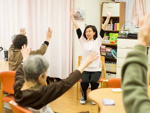 機能訓練の様子 機能訓練室 ゆったりとした空間で体操をしている方々です。手を挙げて、明るい雰囲気の中で健康維持に励んでいます。