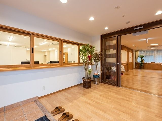 明るい玄関と受付 ロビー   木目の床が広がる明るいロビーです。受付窓口が見え、落ち着いた出入り空間になっています。