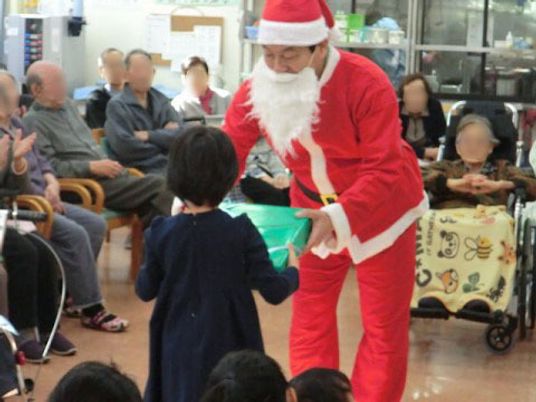 サンタクロースの姿の男性が、女の子にプレゼントを渡している様子である。地域の人々との交流を深めながらクリスマス会が行われている。