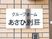 玄関出入口横の薄い茶系のタイル調の外壁の上に掲げられた表札で、白色のプレートに黒文字で施設名が書かれている。