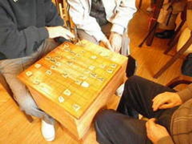 将棋を囲む人々 ラウンジ リラックスした雰囲気の中、入居者たちが将棋を楽しんでいます。コミュニケーションが活発に行われています。