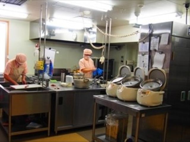 調理中のスタッフの居る厨房 厨房 手際よく調理するスタッフが見える清潔なキッチンです。新鮮な食材で栄養満点の食事を提供しております。