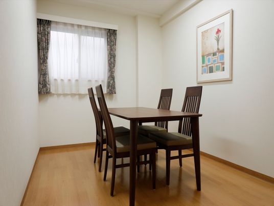 深茶色の椅子とテーブルが並んでいる。窓が１か所備わっている。壁には絵が飾られている。床には障害になるものが置かれていない。