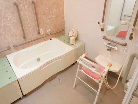 浴室に、背もたれがついた椅子や、浴槽に入る際に腰かける台が置かれている。洗い場や浴槽周りに大きな手すりがいくつも設置されている。