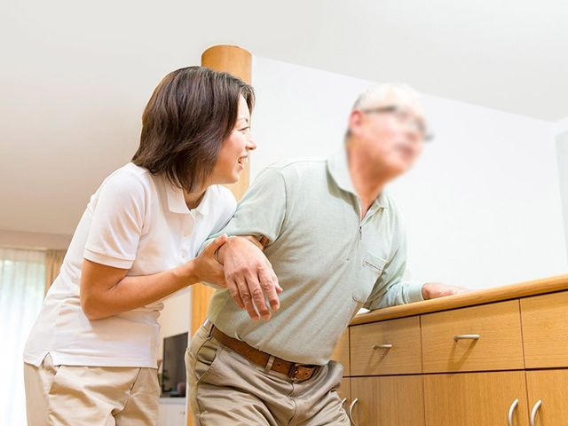 支援するスタッフの様子 リビング 広々とした明るい空間で、スタッフが利用者を丁寧に支援しています。温かみのある環境です。