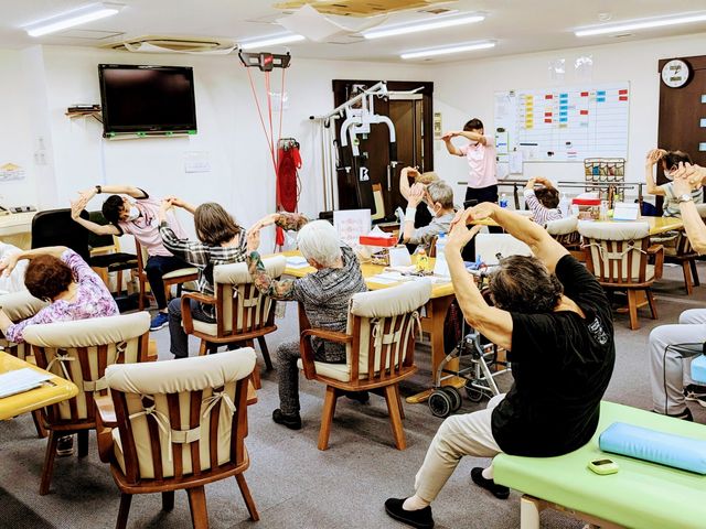 体操中の部屋 機能訓練室 利用者の皆様がスタッフと一緒に体操を行っています。アットホームな雰囲気の中で健康をサポートします。