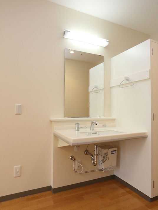 居室に設けられている大きな鏡付きの洗面台。洗面道具を置くスペースもある。向かって右のクロ―ゼットの壁にタオル用ハンガーが付いている。