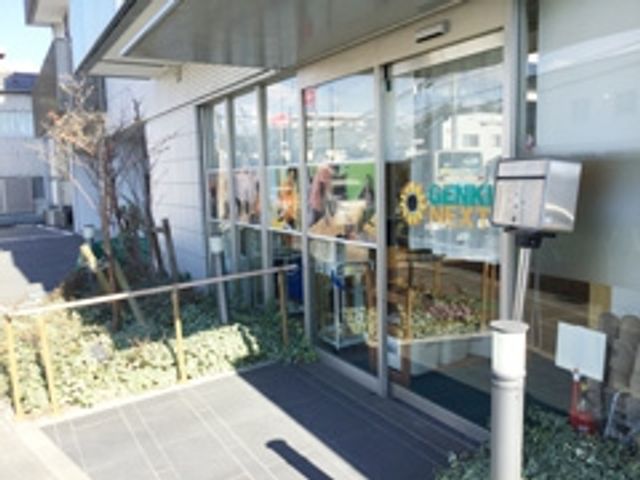 看板付きのエントランス エントランス 広々としたエントランスはガラス扉で明るく、来訪者を快適に迎え入れます。植物も配置されています。