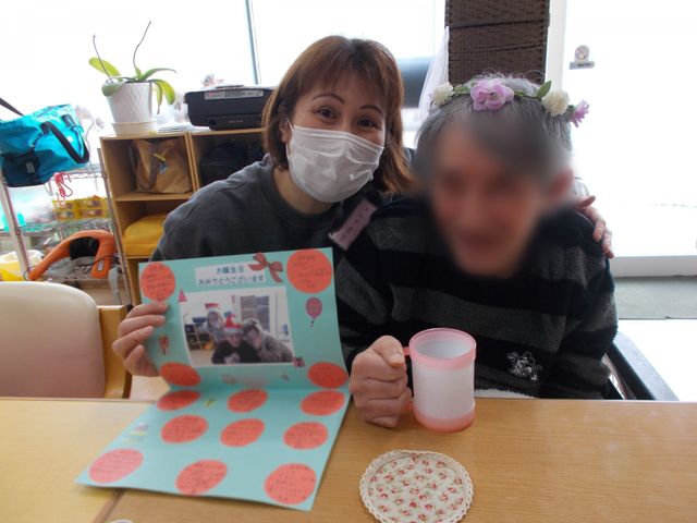 笑顔で本を見せるスタッフ 居室 スタッフが利用者様と共に、リラックスした雰囲気の中で本を楽しんでいます。