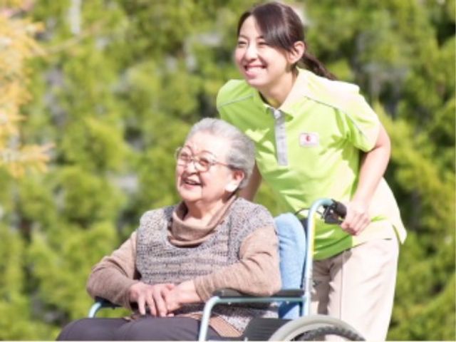 笑顔のスタッフと利用者 日常 穏やかな空気が感じられる光景です。スタッフが利用者を優しくサポートしており、明るい表情が印象的です。