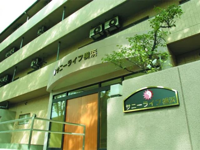 建物外観の入口 外観   明るい色合いの建物外観で、入口まわりはすっきりした印象です。看板も見え、初めて訪れる方にもわかりやすいです。