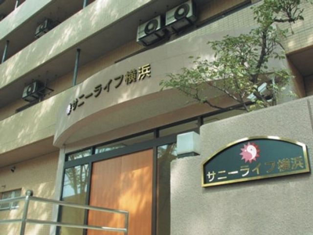 入り口のエントランス看板 施設外観 木の扉が特徴的な明るいエントランスで、訪れる方を温かく迎えます。エントランスには案内板も設置され、訪問者にとって分かりやすい造りとなっています。