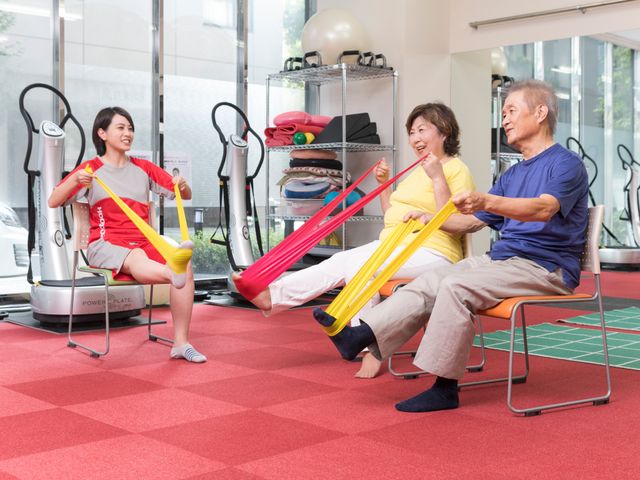 機能訓練室での活動風景 明るい訓練室にて、笑顔でリハビリをする様子が伝わります。スタッフの指導の下、一人一人に合った運動が行われているようです。