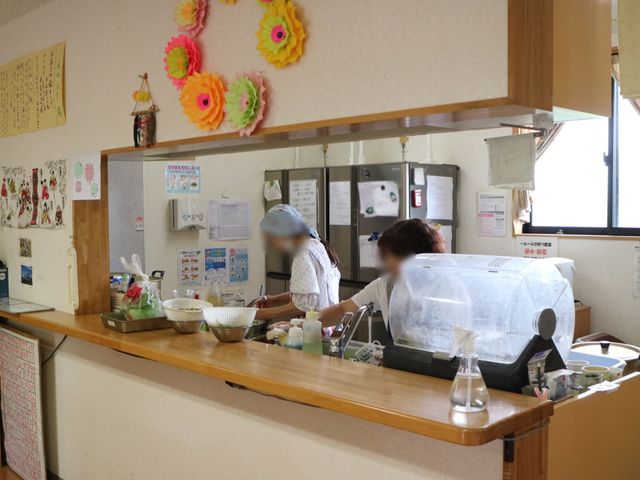 施設のダイニングカウンター キッチン 明るく清潔感のあふれる食堂カウンターです。手際よく立ち働くスタッフの姿が見受けられ、活気があります。