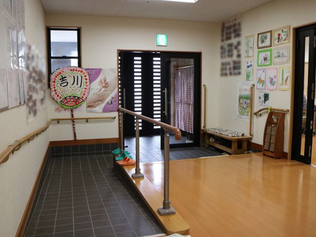 廊下に飾られる掲示物 玄関 手すりが設置された安全な歩行空間です。壁には様々な季節のイベントが描かれた作品が飾られ、温かみのある雰囲気を演出しています。