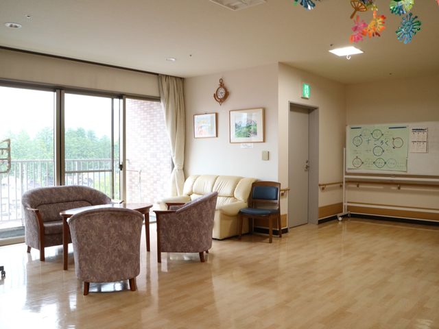 清潔な居間の一角 リビングダイニング ゆったりとしたソファが配置され、窓外の明るさが心地よい空間です。壁には案内図や芸術的な飾りがあります。