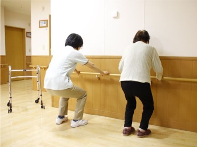 歩行訓練を行う廊下 トレーニング 職員が支えながら歩行練習をしている場面です。温かみのある壁と広々とした空間で、リハビリに取り組んでいらっしゃいます。