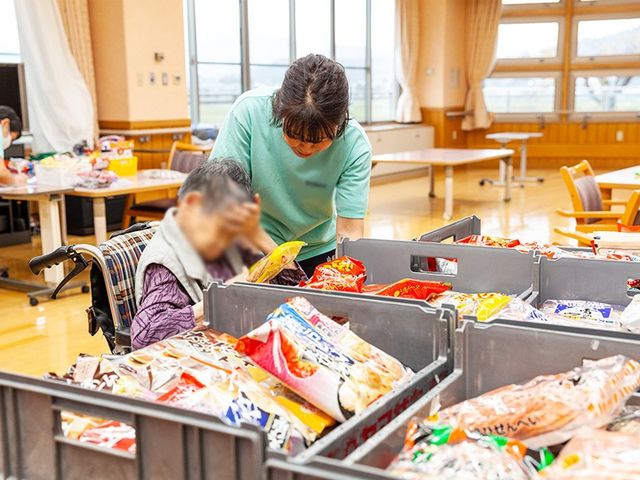 食事準備を手伝うスタッフと利用者さんの様子 ダイニングルーム 広々とした明るいスペースで、スタッフが利用者さんをサポートしています。和やかな雰囲気です。
