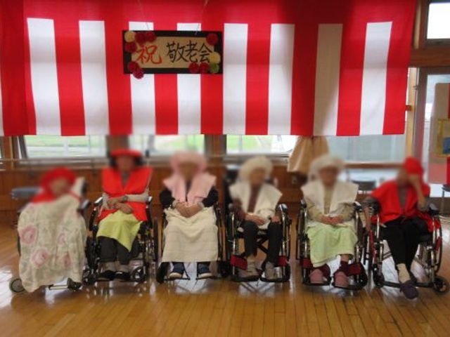 敬老会の様子 多目的室 敬老会で、車椅子の利用者の方々が並んでいます。祭りの雰囲気が感じられる場です。