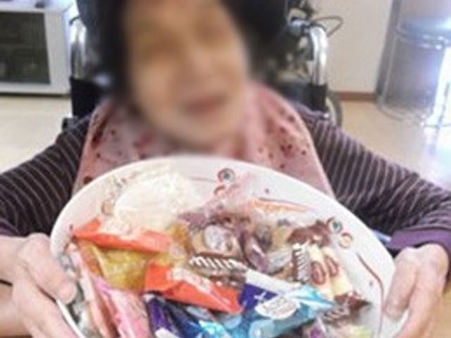 笑顔の利用者とお菓子 ダイニングルーム お菓子を持つ利用者が、笑顔でくつろぎのひとときを過ごされています。
