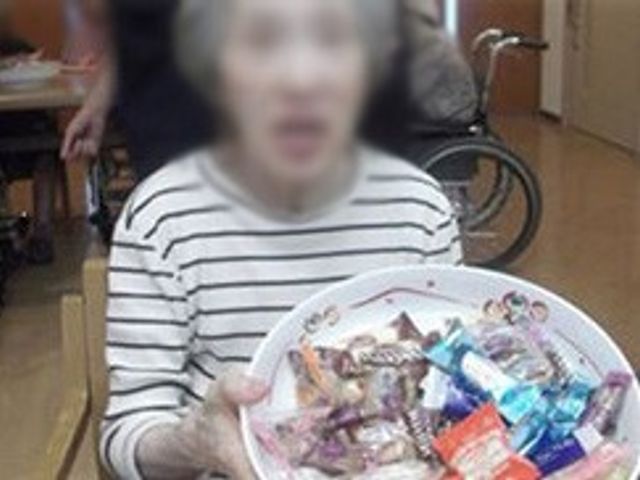 お菓子を持つ女性 食堂 お菓子を手にした女性が、交流を楽しむ空間です。背後には車椅子の方も見られます。