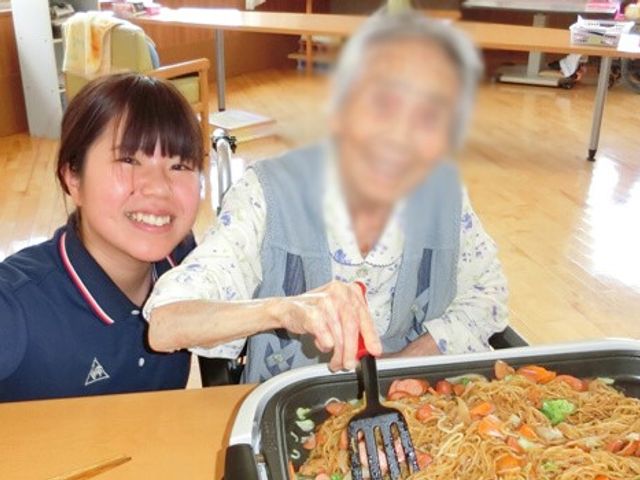 笑顔のサポート風景 ダイニングルーム 広々とした空間で、利用者とスタッフが笑顔で調理を楽しむ場面です。