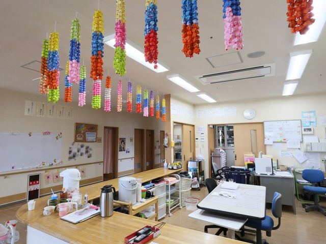カラフルな飾りの多目的室 事務室 天井にカラフルな飾りがある広々とした空間です。デスク周りは整理されており、様々な活動が行える環境が整っています。