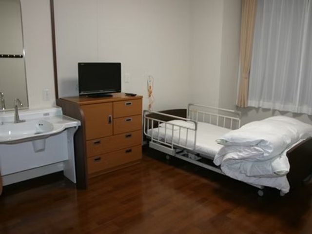 居室のベッドと洗面台 居室   木目調の床が落ち着いた印象の個室です。洗面台とテレビ、ベッドがあり、静かに過ごしやすそうです。