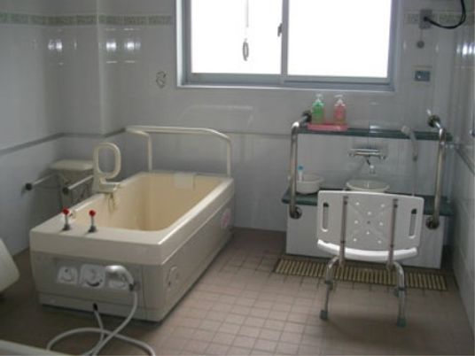 壁が白色の清潔感ある浴室である。介護専用の浴槽が備え付けられており、安全に入浴できるようグリップや手すりがついている。