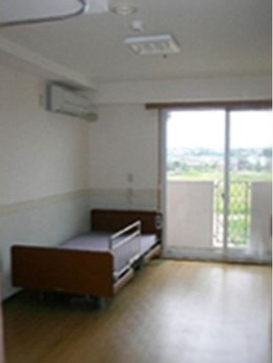 茶色のベッドやエアコンが完備された、シンプルな居室である。掃き出し窓を設置しており、日当たりや風の通りがよい。