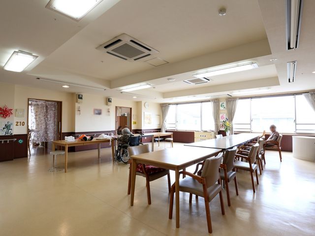 広々とした明るい食堂 共有スペース ゆったりとした空間の食堂では、ご入居者がお食事や会話を楽しまれています。窓辺に座る方々が穏やかな時間を過ごしている様子が伺えます。