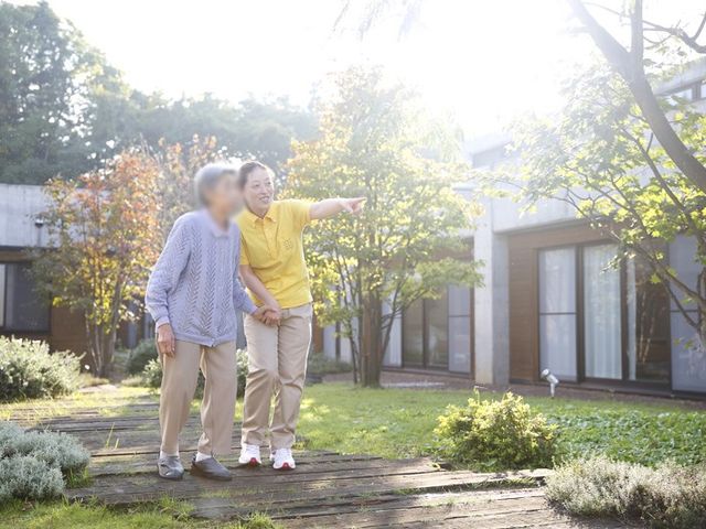 庭を散策する人々 庭 自然光が降り注ぐ庭で、スタッフが入居者と一緒に散策を楽しんでいます。リラックスした雰囲気が感じられます。