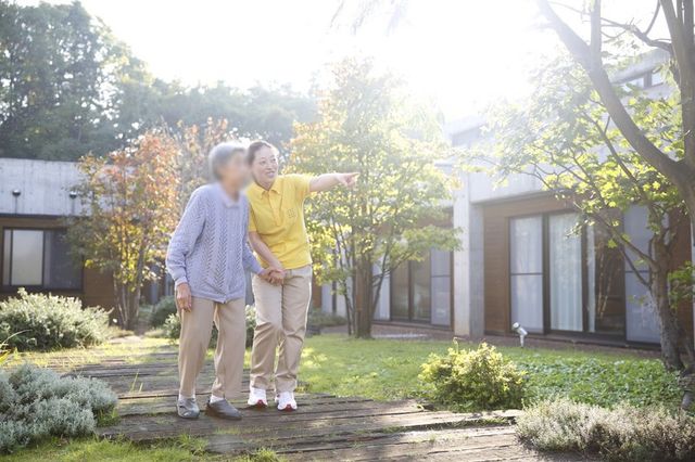庭を散策する人々 庭 自然光が降り注ぐ庭で、スタッフが入居者と一緒に散策を楽しんでいます。リラックスした雰囲気が感じられます。