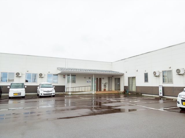 清潔感のある建物エントランス 外観 ゆとりある駐車場を備えた、明るい外観の建物です。障がい者用駐車スペースも設けられ、バリアフリーへの配慮が見られます。