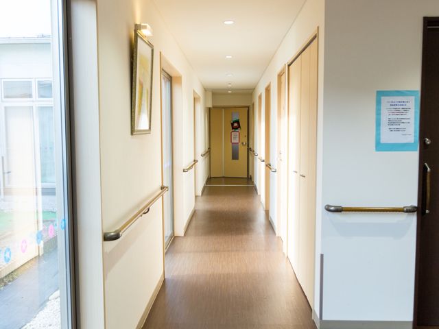 廊下の明るい風景 廊下 手すりが設置された広々とした通路です。壁には絵が飾られ、温かみのある雰囲気が漂っています。