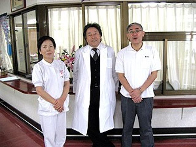 3人が並ぶロビー ロビー   白衣のスタッフ2人と男性1人が、窓際の明るいロビーに並んで立っています。受付まわりのような落ち着いた空間で、来訪時の印象が伝わります。