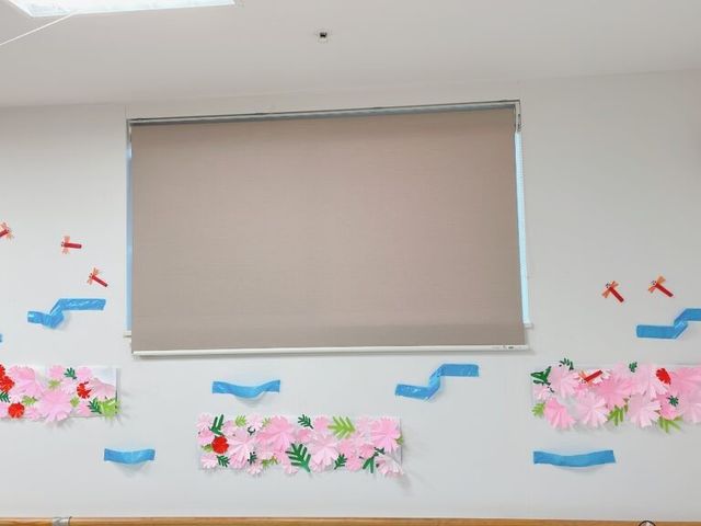 装飾された掲示壁 掲示物   やさしい色合いの花飾りが並ぶ壁面です。明るく親しみやすい空間づくりが感じられます。