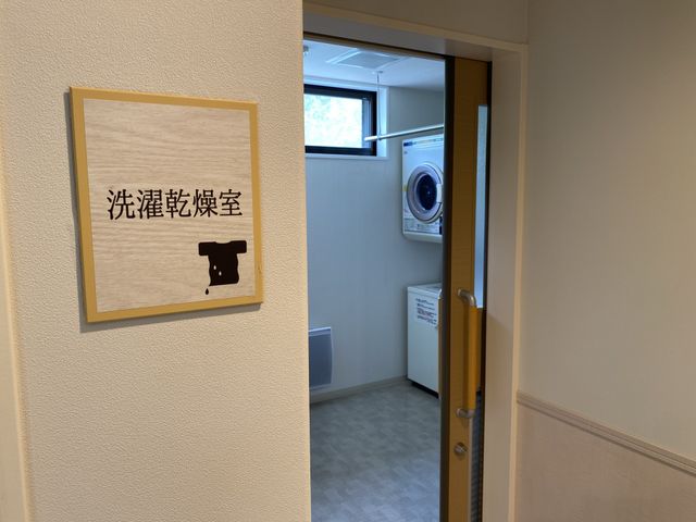 洗濯機が見える廊下 コインランドリー 清潔感のある廊下の突き当たりには、洗濯機が設置されたスペースがあります。利用者の日常生活をサポートする設備が整っています。