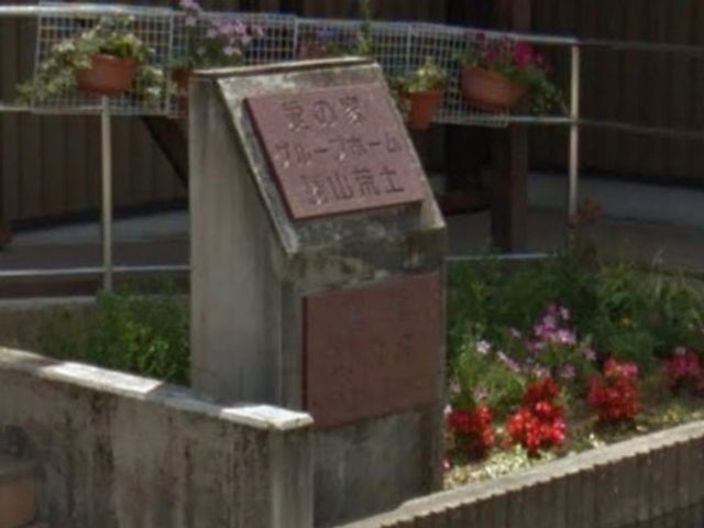 施設の看板と花壇 看板 暖かな印象の施設入口には花々が彩りを添え、来訪者をやさしく迎えています。