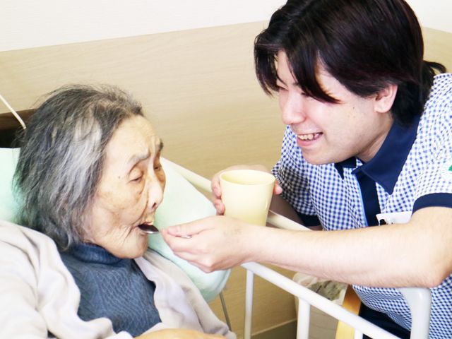 笑顔のスタッフと高齢者 居室 スタッフが親身に介助する場面です。一人ひとりに寄り添ったケアが行われています。
