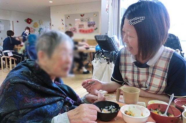 スタッフと笑顔の時間 ラウンジ 利用者が職員と親しげに会話を楽しんでいます。暖かみのある空間で、和やかなひとときを過ごせます。