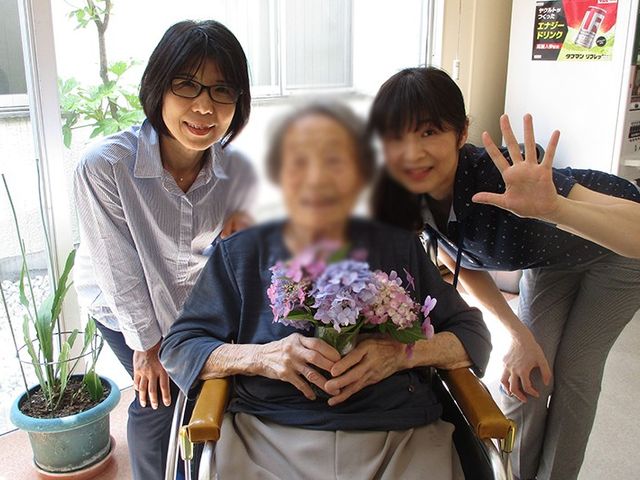 和やかなスタッフと居住者 リビング 自然光が差し込む暖かな雰囲気の中で、笑顔のスタッフが居住者をサポートしています。