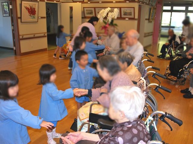 交流する子どもたちと利用者たち 内観 子どもたちとの交流が行われ、明るい笑顔があふれる温かい雰囲気です。協力し合う場面が魅力的です。