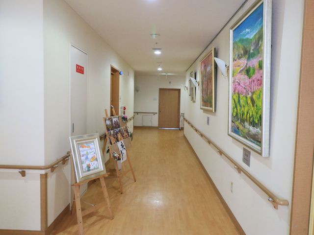 明るい廊下と絵画 廊下 手すりが設置されたきれいな廊下です。壁に掛けられた絵や設置されたイーゼルが、温かみのある雰囲気を演出しています。