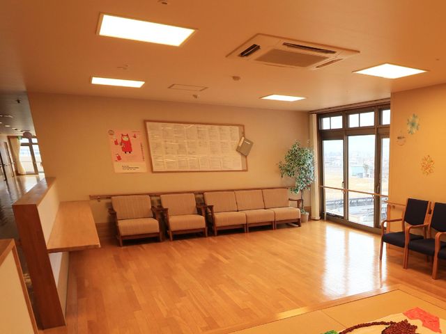 明るい待合室の全景 共有スペース ゆったりとしたソファが並ぶ待合室です。窓辺には植物が置かれ、柔らかな光が差し込む安らぎの空間となっています。