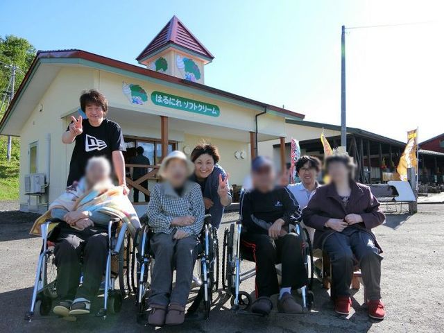 家の前で笑顔の人々 外観 和やかな雰囲気の中、スタッフと利用者らしき人々が家の前で楽しそうに過ごしています。